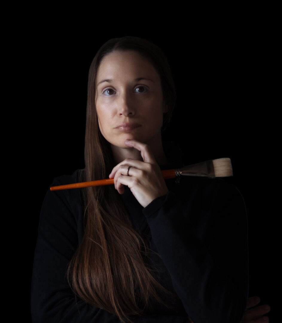 A woman holding a brush and looking at the camera.