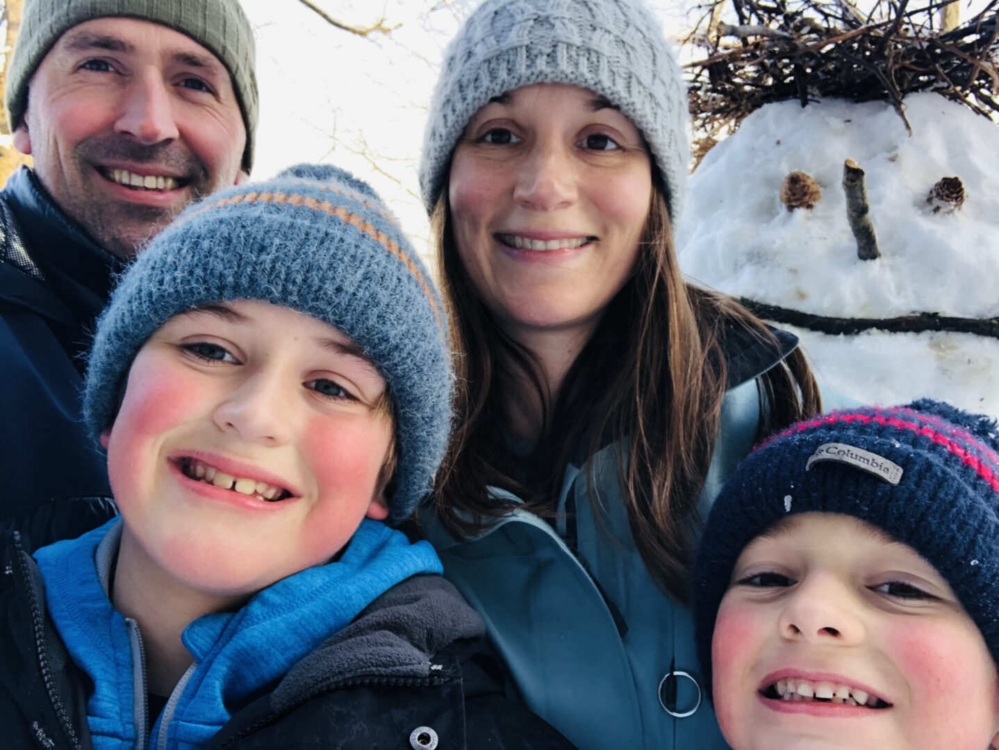 A family poses for a picture in front of a snowman.
