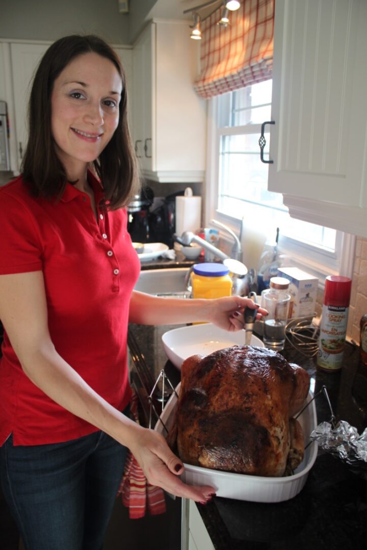 A woman in red shirt holding turkey on the grill.